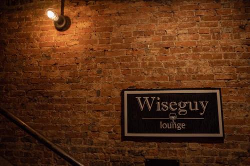 A dimly lit brick wall featuring a sign that reads "Wiseguy Lounge."