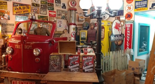 A vintage fire truck surrounded by retro signs, gas pumps, and memorabilia in a nostalgic display.