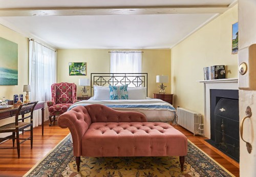 Cozy bedroom featuring a large bed, pink chaise lounge, desk, and decorative artwork on yellow walls.