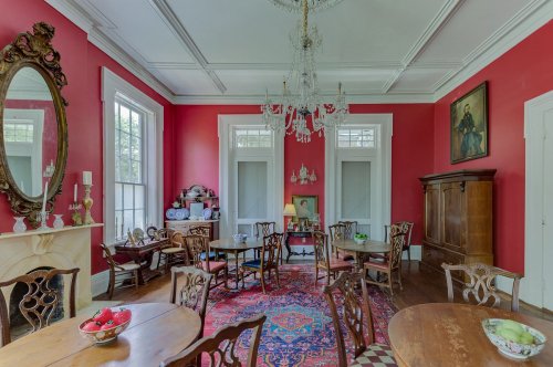 Elegant dining room with red walls, chandelier, antique furniture, and a decorative rug.