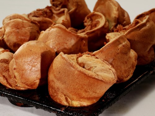 A close-up of golden-brown Yorkshire puddings arranged on a baking tray.