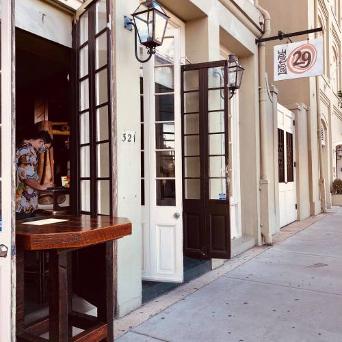 A street view of a building with open doors, a wooden table outside, and a person inside.