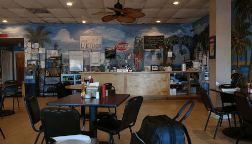 A casual dining area with black chairs, a wooden counter, and a tropical mural on the wall.