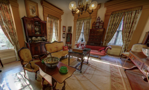 A vintage room with ornate furniture, curtains, and decorative items, featuring a chandelier and warm lighting.