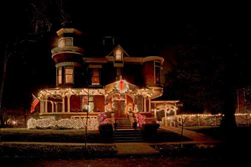 A beautifully decorated Victorian house at night, adorned with festive lights and holiday decorations.