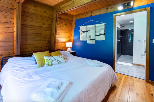 Cozy bedroom with a wooden interior, a bed with white linens, and a bathroom visible in the background.