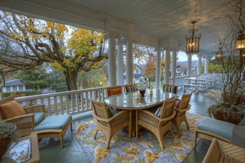 A cozy porch with wicker furniture, a round table, and autumn foliage visible through the columns.