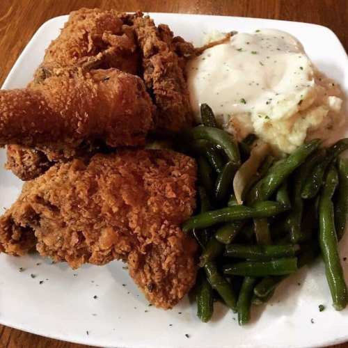 A plate of crispy fried chicken, creamy mashed potatoes with gravy, and green beans.