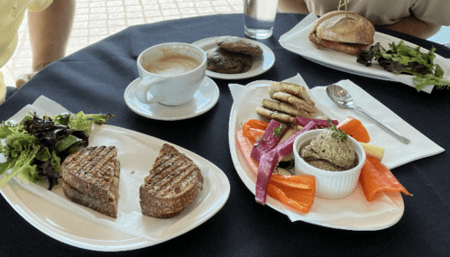 A table setting with two plates of food: grilled sandwiches, a platter of vegetables, and a cup of coffee.