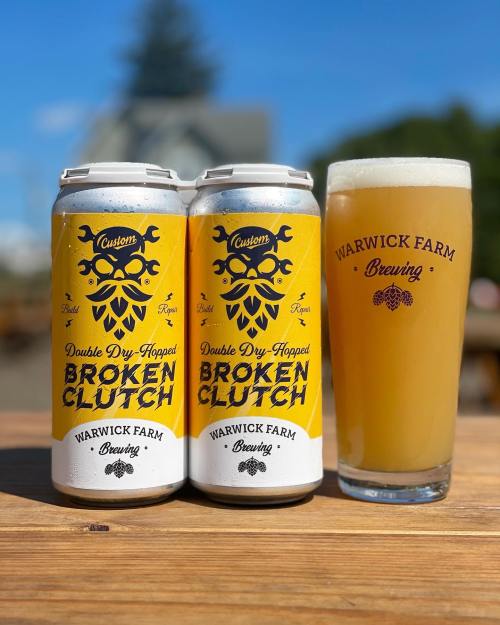 Two cans of "Broken Clutch" beer from Warwick Farm Brewing next to a glass of the same beer on a wooden table.