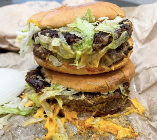 A stacked burger with melted cheese, lettuce, and a toasted bun, resting on crumpled paper.