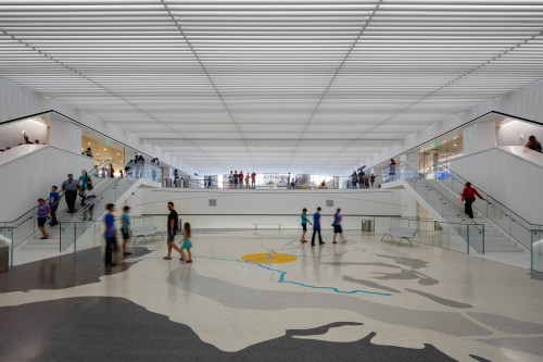 A spacious, modern interior with people walking on multiple levels, featuring a large mural on the floor.