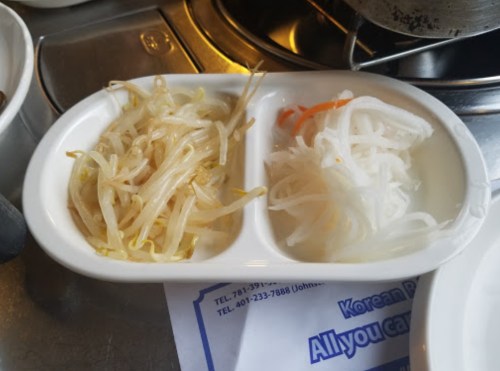 A white dish divided into two sections, one with bean sprouts and the other with pickled radish.