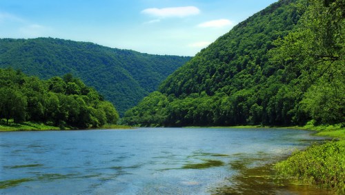 A serene river flows between lush green hills under a clear blue sky.