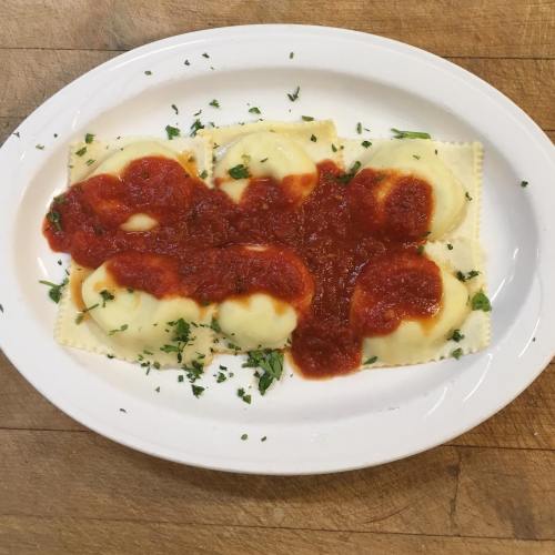 Plate of ravioli topped with marinara sauce and sprinkled with fresh herbs on a wooden surface.