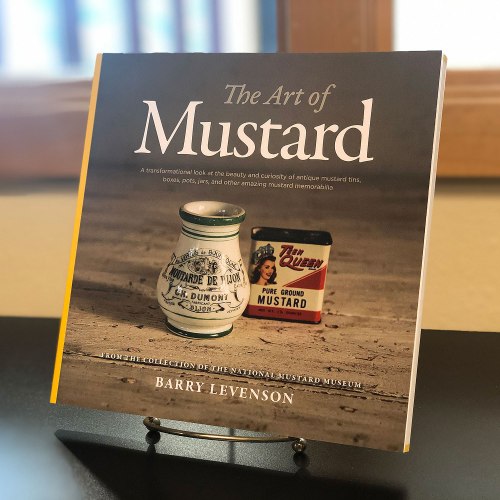 Book titled "The Art of Mustard" by Barry Levenson, featuring antique mustard tins on display.