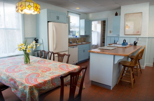 Bright kitchen with a dining table, floral centerpiece, light blue cabinets, and a cozy atmosphere.