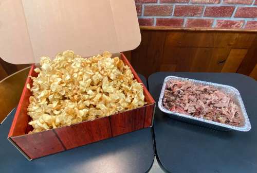 A large box of golden popcorn next to a tray of shredded meat on a table.