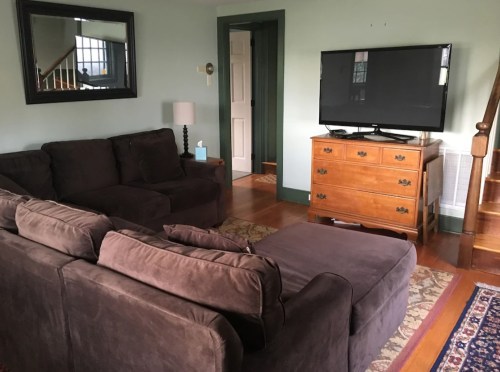 Cozy living room with a brown sectional sofa, wooden TV stand, and a door leading to another room.