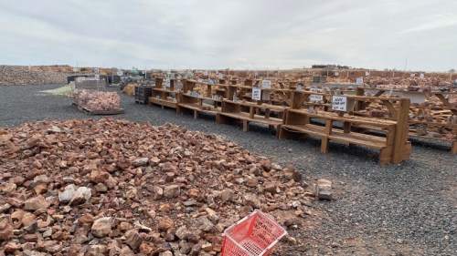A rocky landscape with wooden shelves displaying items, surrounded by piles of stones and a shopping cart.