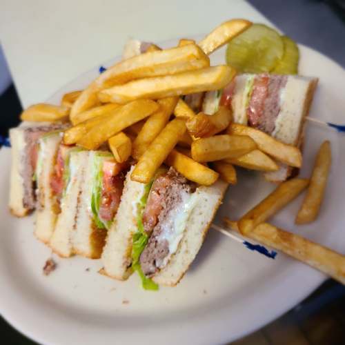 A plate with a layered sandwich filled with lettuce, tomato, and meat, accompanied by a side of French fries and a pickle.