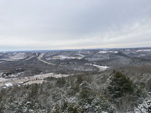 A snowy landscape with rolling hills, a winding road, and a cloudy sky in the distance.