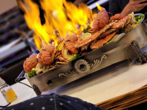 A large seafood platter with lobsters and crabs, surrounded by flames, served on a decorative metal tray.
