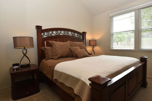 Cozy bedroom featuring a wooden bed, brown bedding, and two bedside lamps with a window letting in natural light.