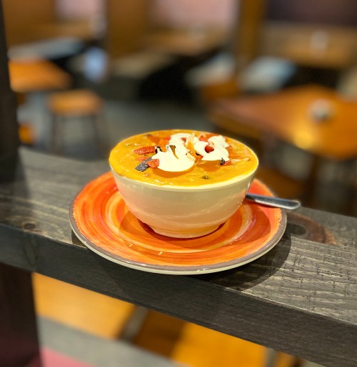 A bowl of soup topped with cream and garnished with berries, resting on a colorful plate on a wooden table.