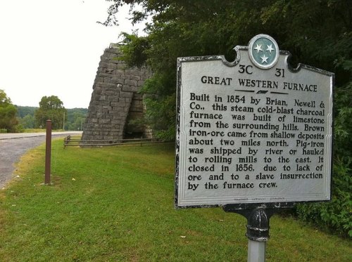 Sign for Great Western Furnace, built in 1854, with a stone structure in the background and trees lining the road.