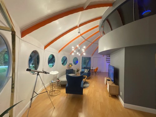 Modern interior with curved ceiling, large circular windows, a telescope, and stylish furniture in a cozy living space.
