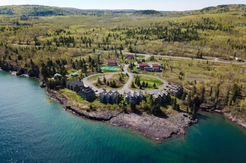 Aerial view of a coastal resort with buildings surrounded by greenery and water, set against a scenic landscape.