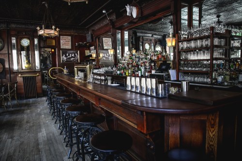 A vintage bar interior with a long wooden counter, shelves of liquor, and elegant decor in a dimly lit setting.