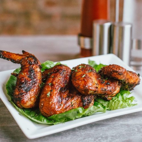 A plate of grilled chicken wings garnished with lettuce, served on a wooden table.