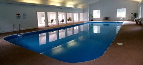 Indoor swimming pool with clear blue water, surrounded by chairs and large windows letting in natural light.