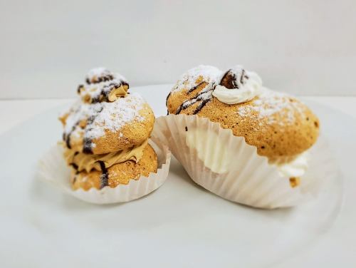 Two cream-filled pastries topped with powdered sugar and chocolate drizzle, placed on a white plate.