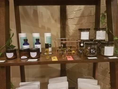 A wooden shelf displaying various jars and bottles of herbal products and oils, with labels and colorful tags.