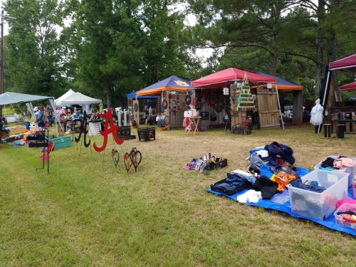 A vibrant outdoor market with colorful tents, various goods for sale, and clothing displayed on the grass.