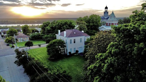 Aerial view of a scenic landscape featuring a historic building, lush greenery, and a sunset over the horizon.