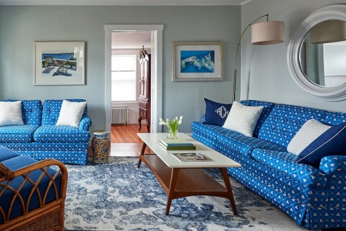 A cozy living room featuring blue patterned sofas, a white coffee table, and decorative art on the walls.