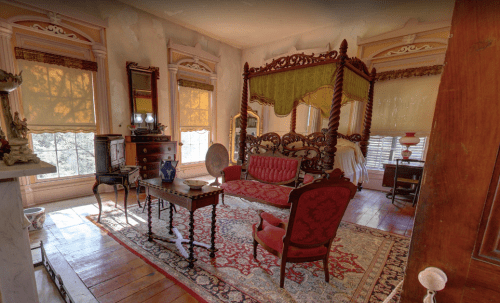 Victorian-style room with a four-poster bed, ornate furniture, and warm lighting, featuring a patterned rug and vintage decor.