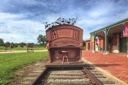 A vintage train car with musical notes on top, positioned on tracks near a brick path and green grass.