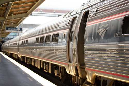 Amtrak train at a station, showcasing sleek silver exterior and logo, with platform and sign in the background.