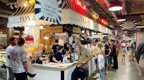 A bustling food market with people lining up at various stalls, enjoying a vibrant atmosphere and diverse food options.