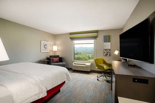 A modern hotel room featuring a bed, chair, desk, and large window with mountain views.