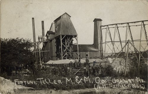 Historic black-and-white photo of a fortune teller's building with a wooden structure and mining equipment in the background.