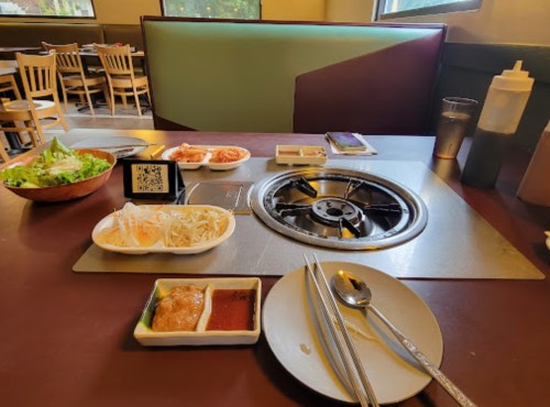 A dining table set for a meal with a grill, side dishes, and utensils, in a restaurant setting.