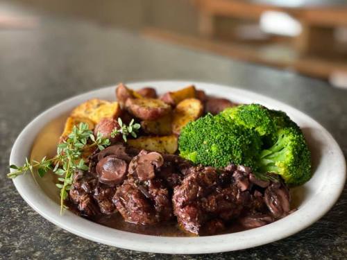 A plate of tender beef with mushroom sauce, roasted potatoes, and steamed broccoli, garnished with fresh herbs.