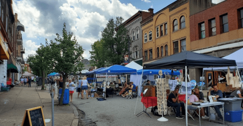 A bustling street market with tents, vendors, and people enjoying the day under a partly cloudy sky.