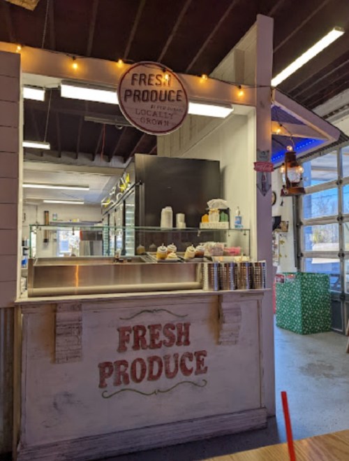 A rustic produce stand with a sign reading "Fresh Produce," featuring shelves and a display of various items.